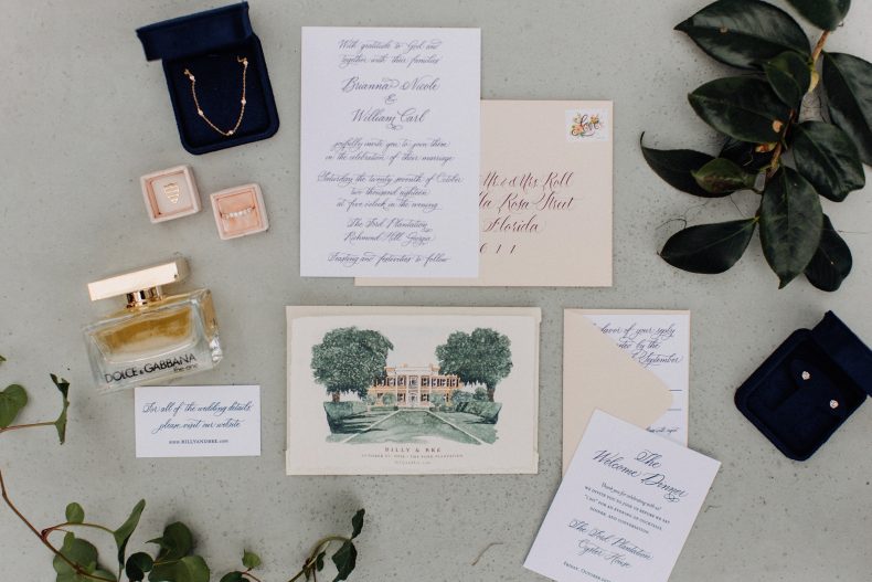 arrangement of things laying on ground including wedding invitation with watercolor of ford plantation on front